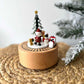 Wooden Christmas decoration with Santa Claus, snowman, and tree on a woven surface.