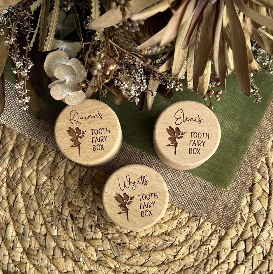 Three wooden tooth fairy boxes with engraved names on a decorative background