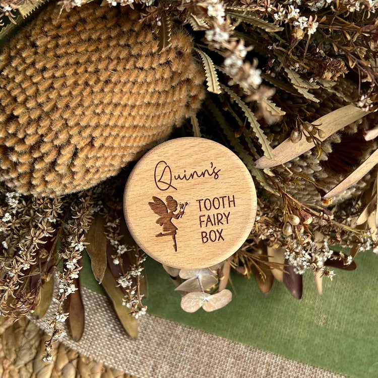 Wooden tooth fairy box with engraved text, surrounded by dried flowers and leaves.